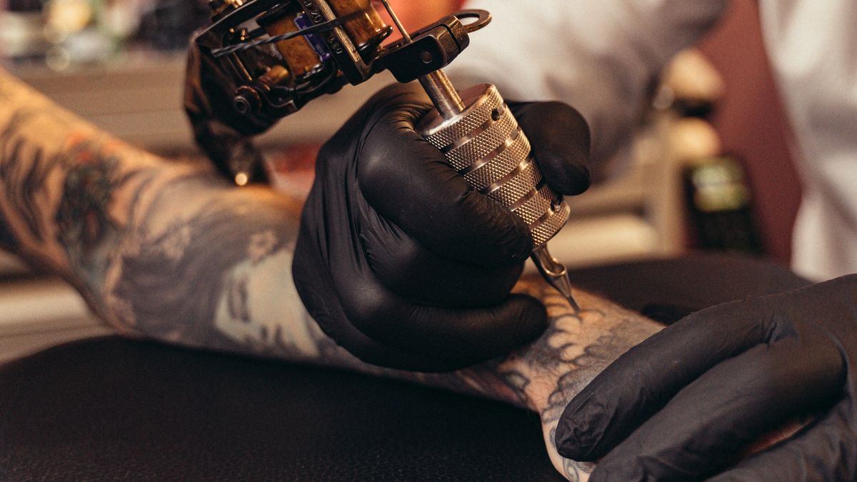 Tattoo artist wearing black gloves working on client with tattoo machine