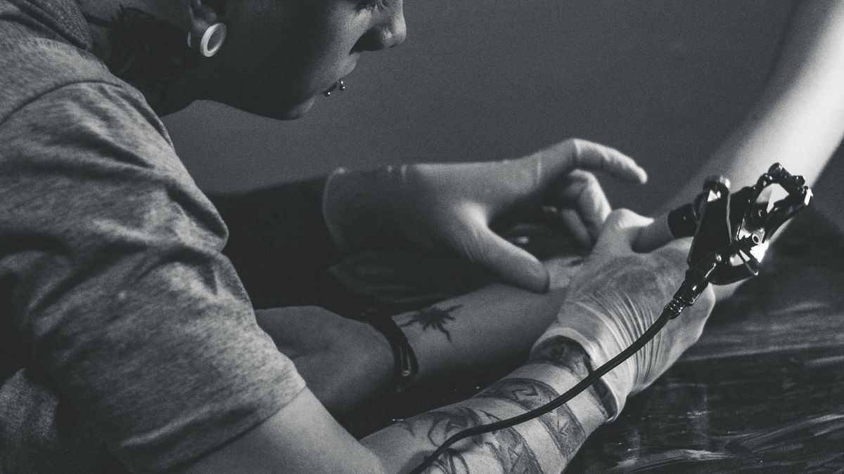 Tattoo artist wearing black gloves working on client's back with a tattoo machine