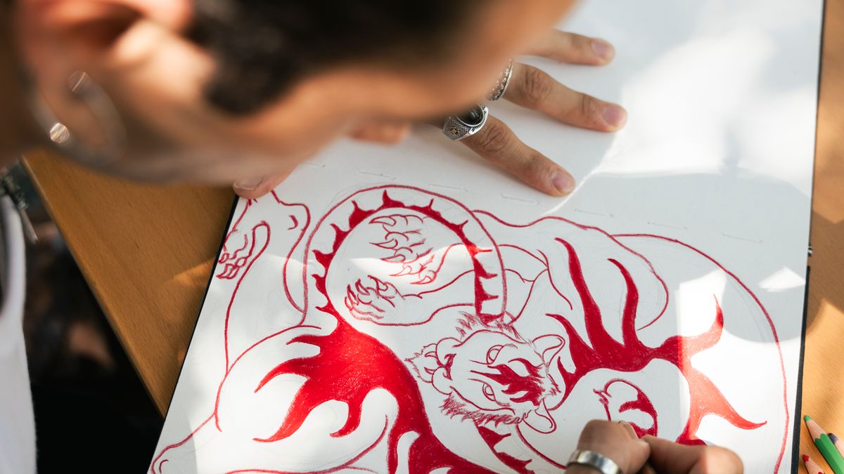Artist sketching an intricate dragon tattoo design on paper from above